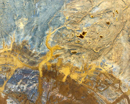 Aerial view of the abstract textures and vibrant yellow mineral deposits in the open-pit mining landscape of Minas de Riotinto, Andalusia, Spain.