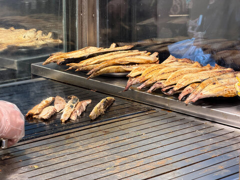 Grilled fish fillets cook on hot metal griddle for balik ekmek preparation in Istanbul street food kitchen with glass counter. Turkish food, seafood menu, culinary tourism, restaurant