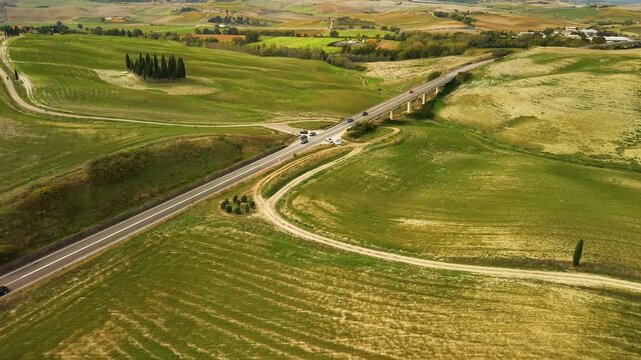 Italy Tuscany Val d'Orcia cypresses aerial 4K drone road cars , wide green hills low top down flyover over cypress grove revealing dirt path countryside landscape cinematic overflight