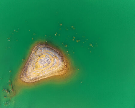 Aerial view of the unique concentric rock formations of a small island surrounded by vibrant emerald green water at the mining site Minas de Riotinto, Andalusia, Spain.