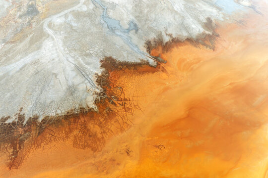 Aerial view of the Minas de Riotinto showing vibrant orange acidic water and cracked earth patterns with white mineral deposits in Minas de Riotinto, Andalusia, Spain.
