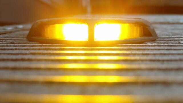A flashing orange warning light on a metal step surface, alternating between bright glow and off.