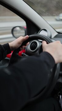 Vertical screen young man driving car through urban traffic realistic transportation lifestyle hands on steering wheel during everyday commute in modern city
