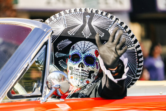EL PASO, TEXAS &ndash; NOVEMBER 01, 2025: A festival participant wearing a detailed sugar skull mask and embroidered mariachi sombrero waves from a classic red car during a Dia de los Muertos celebration.
