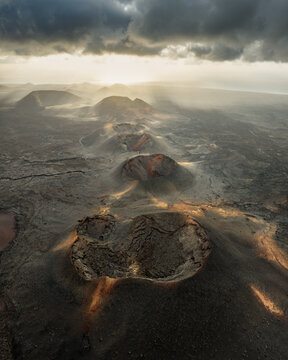 Aerial view of the volcanic craters of Timanfaya National Park and vast lava fields under a dramatic sky with sunbeams in Lanzarote, Canarias, Spain.