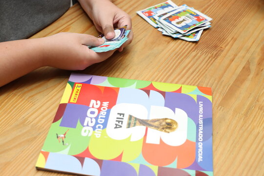A person's hands fan out collectible football player stickers next to the official FIFA World Cup 2026 Panini album