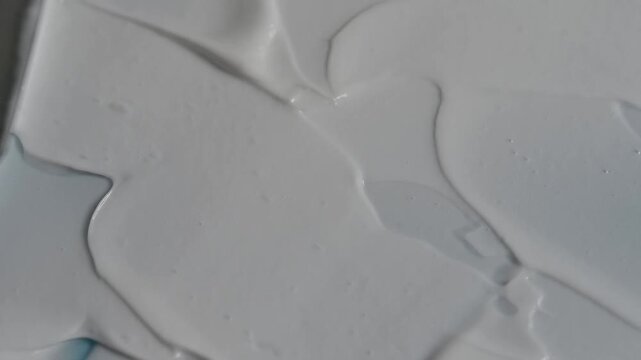 Close up shot of a palette knife mixing and spreading thick white acrylic paint or texture paste on a surface, creating smooth strokes.