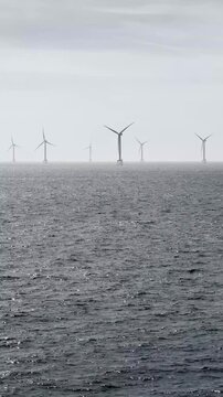 Vertical Offshore Wind Farm Video With Wind Turbines on the Sea Horizon, Moody Grey Sky, Rough Water and Renewable Energy Infrastructure