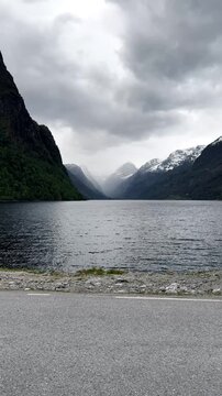 Beautiful Vertical Video of Olden Norway With Peaceful Water, Steep Mountain Slopes, Snowy Peaks and Cloudy Fjord Valley Scenery