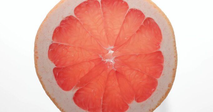 Macro top view close-up shot of a fresh round red grapefruit slice rotating slowly. The vibrant citrus fruit slice spins smoothly, showcasing its juicy pulp, detailed texture, and natural patterns