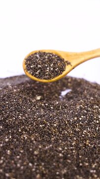 Close up of healthy dry chia seeds being poured from a wooden spoon onto a large mound on bright white background rustic meticulously pours tiny, healthy onto an existing, abundant pile
