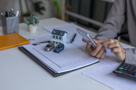 Businessman using a smartphone and reviewing data for financial planning, budgeting for major assets like real estate and vehicles.
