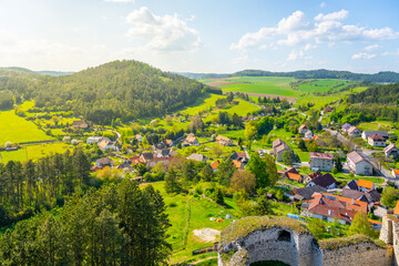 Fototapeta premium The lookout from Rabi Castle shows the green hills and small houses below. Surrounding fields stretch far into the distance under a clear blue sky. Nature and village are visible together.