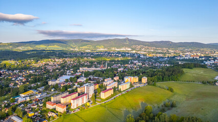 Fototapeta premium Vratislavice nad Nisou with buildings and fields. The sun shines on the town, revealing roads and greenery. Mountains are visible in the background.