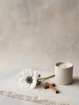 Minimal Christian sympathy card background with white anemone flower, wooden cross and white candle on a pale stone slab, with soft neutral copy space for condolence, memorial or funeral themes.