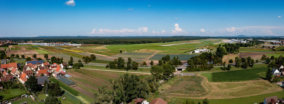 Aerial view of Nuremberg Airport with its runway surrounded by green agricultural fields and village houses under a blue sky in Nuremberg, Bavaria, Germany.