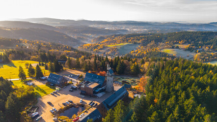 Fototapeta premium Kralovka Lookout Tower stands tall amidst vibrant autumn colors in the Jizera Mountains. Visitors enjoy stunning views in the serene landscape as the season changes.