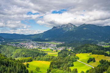 Fototapeta premium Reutte is a town in Tyrol, Austria. This view shows the town and mountains. The area has green fields and forests. Clouds cover part of the sky. It is daytime.