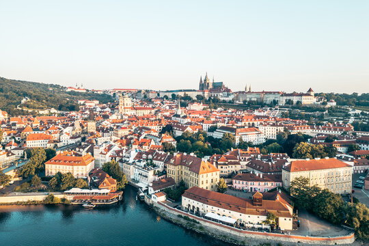 Overlooking the picturesque Lesser Town of Prague, this view showcases charming rooftops along the Vltava River with the majestic Prague Castle rising above the landscape at sunset.