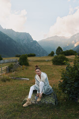 Fototapeta premium Woman lifestyle in nature, sitting on rock, tying boots, casual outfit, mountain valley background, peaceful atmosphere, soft natural light, outdoor activity