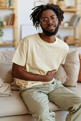 Fototapeta premium Man clutching stomach seated on sofa in cozy living room