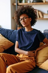 Obraz premium Woman wincing and holding stomach on living room couch