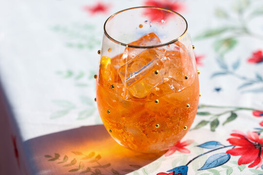 Tropical cocktail in a wine glass. The cold refreshment is orange and is filled with ice cubes. The color is orange. The alcohol beverage is tasty and refreshing on a hot summer day. 