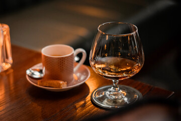Fototapeta premium Glass of Cognac with Coffee Cup on Wooden Bar Counter, Cozy Restaurant Interior Background with Copy Space