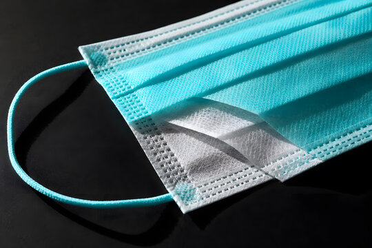 Teal surgical mask showing inner layers on dark background