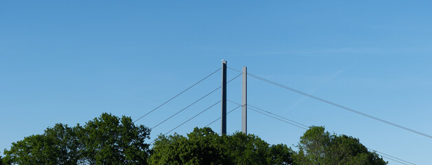Obraz premium Green Trees in Foreground with Suspension Bridge Partially Visible in Background, Nature and Infrastructure Contrast Concept