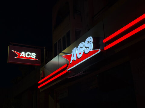 Glowing red and white logo of ACS courier and delivery service on a building facade at night. express delivery and logistics business concept.