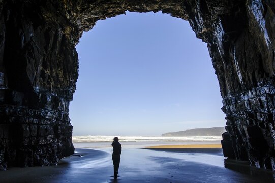 Woman standing in the giant entrance of Cathedral caves in backlit, The Catlins, South Island, New Zealand