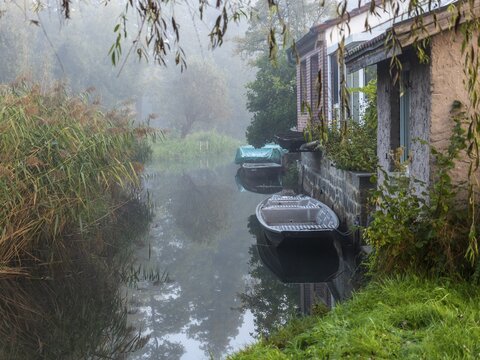 Autumn mist and lonely barges on the Spreewald river, between reeds and the edge of the village, Schlepzig, Spreewald, Brandenburg, Germany