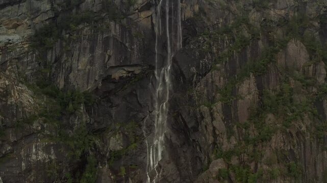 Aerial view of a tall narrow waterfall cascading down a vertical dark rock cliff near Latefossen in Western Norway showing dramatic geological features