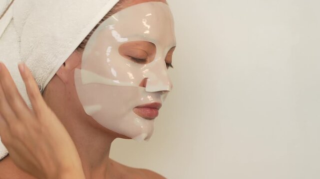 Young woman in a bathroom puts a sheet mask on her face