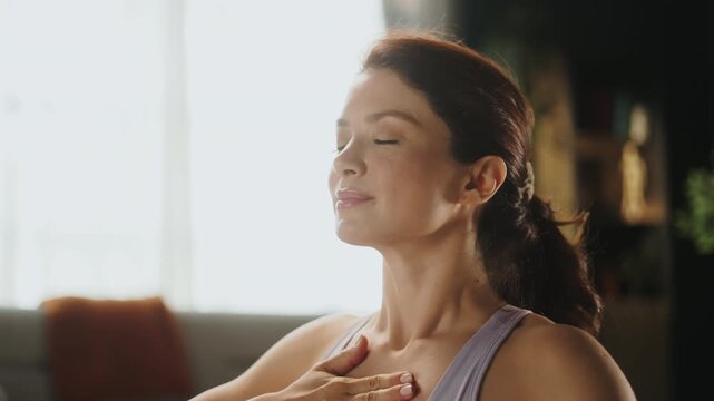 A woman sits calmly in her living room, focusing on her breath and practicing mindfulness. Sunlight fills the space, creating a warm atmosphere for her practice.