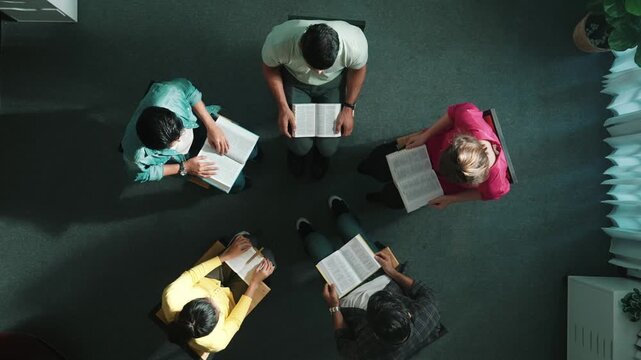 Top view of skilled diverse prayer clasping hand and praying to god while sitting at chair in circle. Top down aerial view of people folded hand while sitting with opened bible on laps. Symposium.