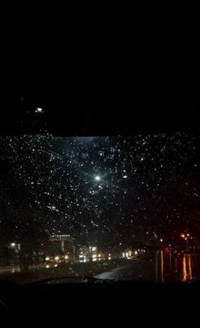 POV shot from inside a car driving at night during heavy rain with windshield wipers working, blurred city lights, relaxing rainy atmosphere, vertical 9:16 video.