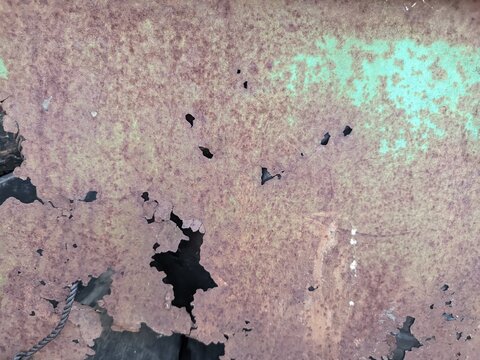 a heavily weathered and oxidized metal surface covered in brown rust, featuring several small and large corrosion holes over fading green paint.
