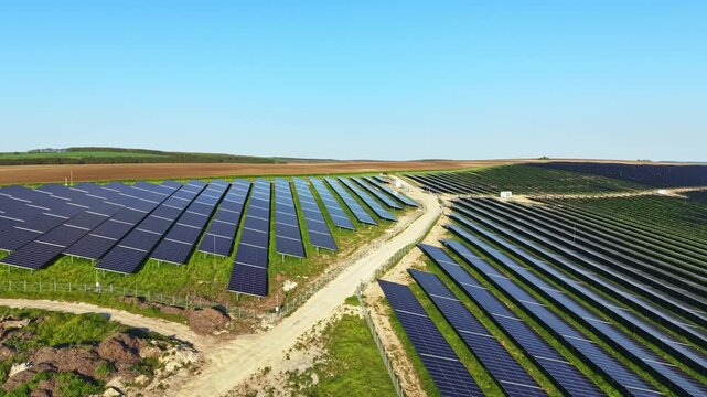 A vast area of solar panels stretches across a green field in the countryside. A dirt road goes through the solar farm on a sunny day. This site shows clean energy efforts in rural development.