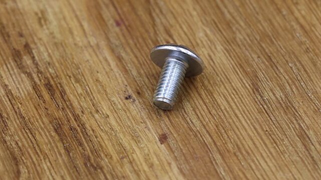 Close-up of a metal screw rotating on a wooden table, showcasing its shiny, metallic surface.