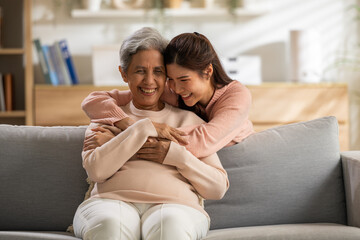 Happy family mother and adult daughter hug with deep love and joyful emotion on sofa in comfortable...