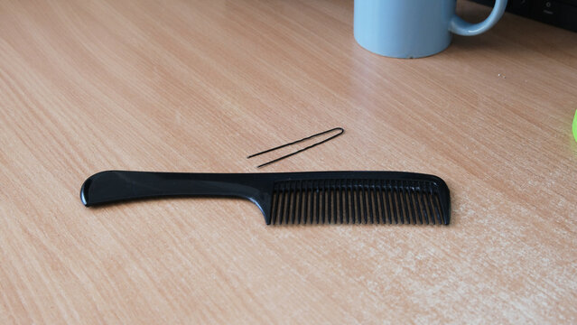 Black plastic comb and metal hairpin on wooden table surface.