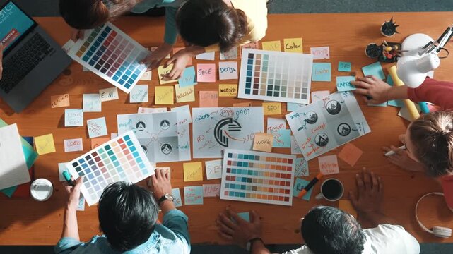 Top down view of designer compare color palettes with laptop and design product. Aerial view of marketing team working together to choose color while discussing about logo graphic design. Symposium.