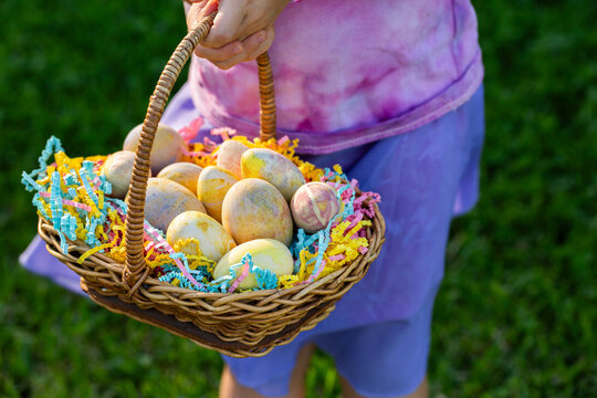 child&rsquo;s hands holding basket of pastel coloured wooden easter eggs in basket outdoors