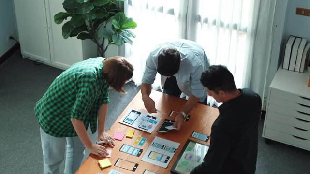 Top view of smart Ui designer brainstorming and planning about Ux Uo design or mobile interface wireframe design with diverse develop team. Caucasian programer walking and joining meeting.Convocation.