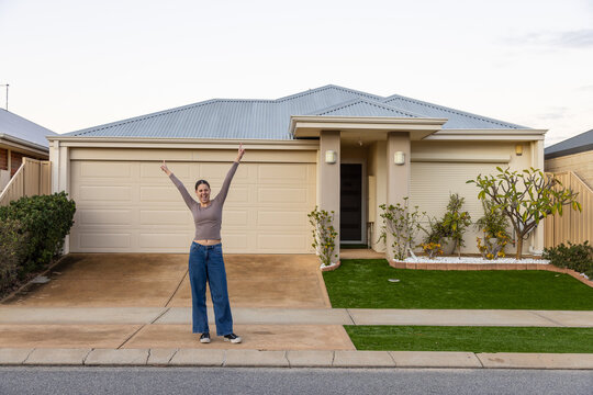 teen girl with arms in the air out the front of a modern suburban house