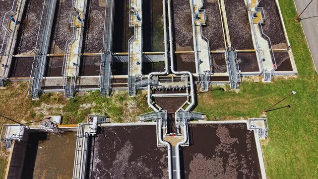 Aerial sewage treatment plant clarifiers aeration basins showing rectangular circular tanks with brown sludge, mechanical scrapers churning, aeration bubbles,