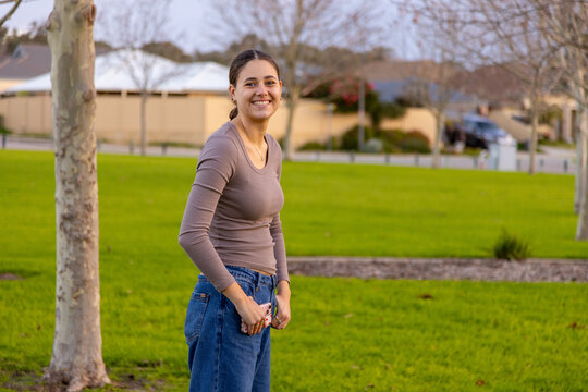 teen girl in suburban park wearing casual clothes with thumbs in pockets