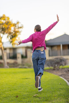 teen girl seen from behind joyfully prancing away leaping in a suburban park